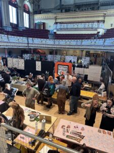 Crowds and live tattooing bays at Huddersfield Tattoo Festival inside Huddersfield Town Hall with the organ backdrop.